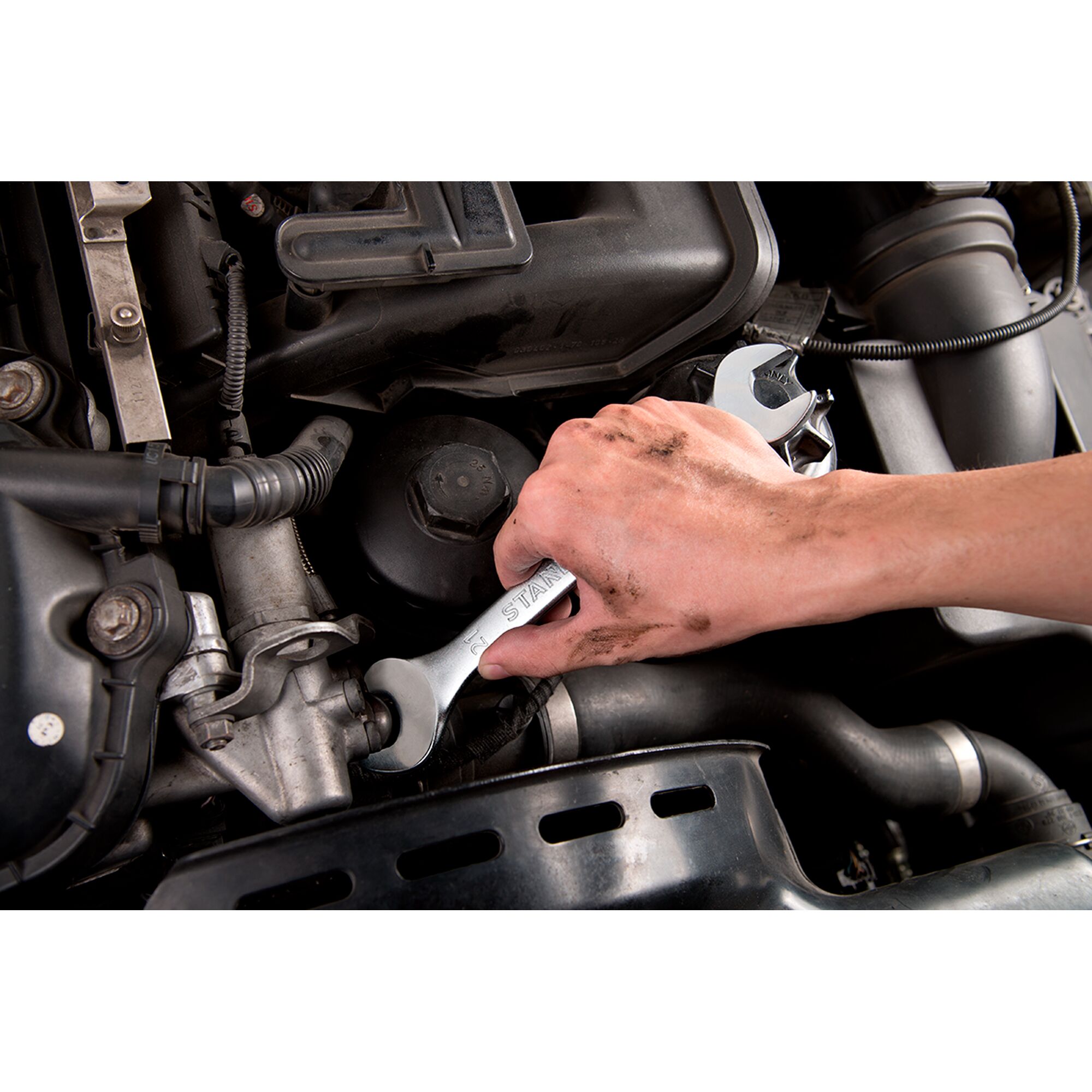 STANLEY STMT23119_BasicWrench being used to loosen a bolt in a car engine compartment, close-up view.
