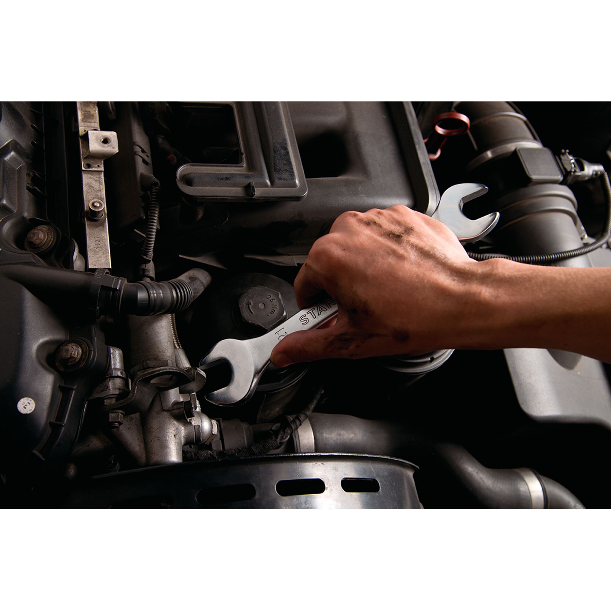 STANLEY STMT23119_BasicWrench being used to tighten a bolt on a car engine, close-up view.