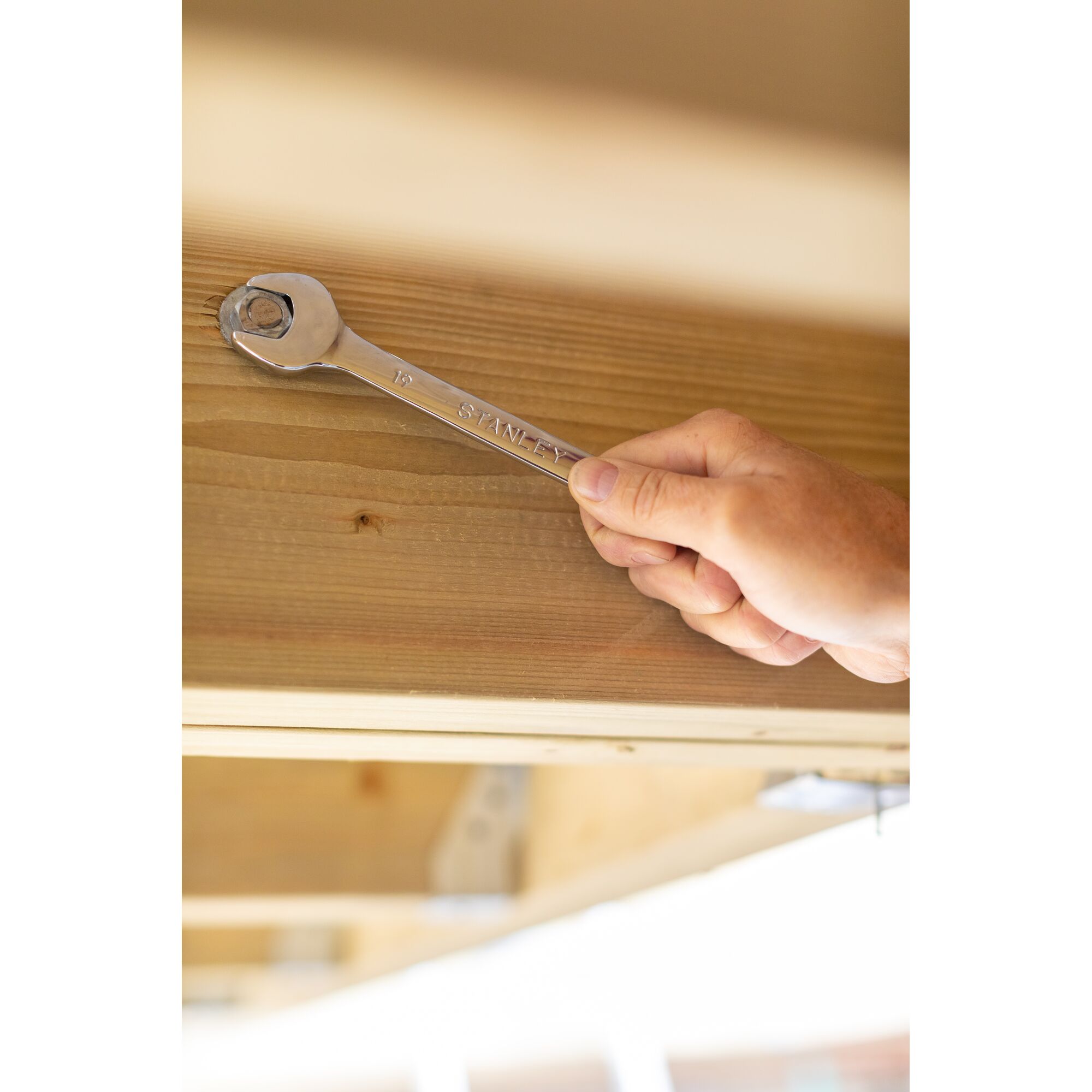 STANLEY STMT95787-0 wrench in use tightening a bolt on wooden beam, close-up photography.